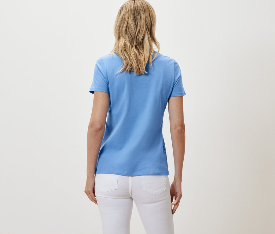 Rückansicht einer Frau in weißen Jeans und einem hellblauen Basic T-Shirt.