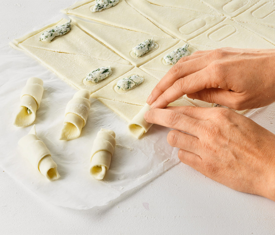 Hände rollen Croissants mit einem Croissant-Roller.