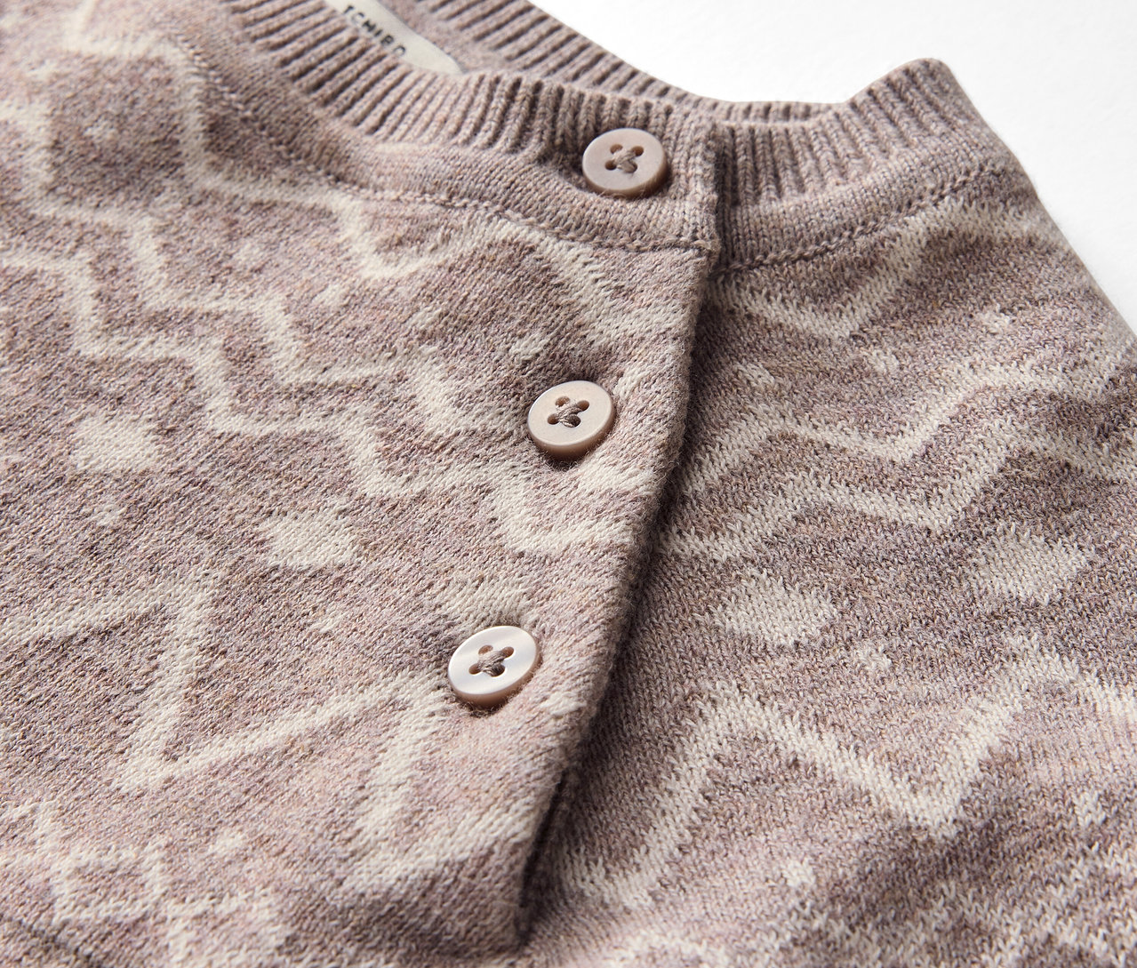 Detailaufnahme eines Strickjacken-Oberteils mit geometrischem Muster und Knöpfen.