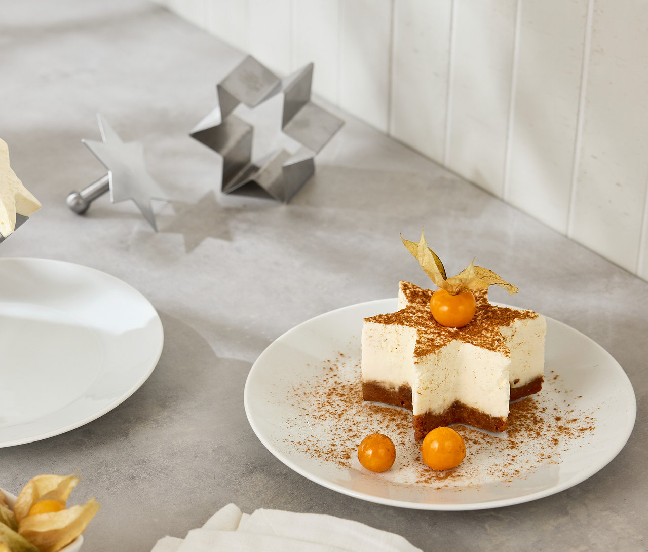 Sternförmiger Kuchen mit Physalis auf einem weißen Teller neben sternförmigen Ausstechformen.