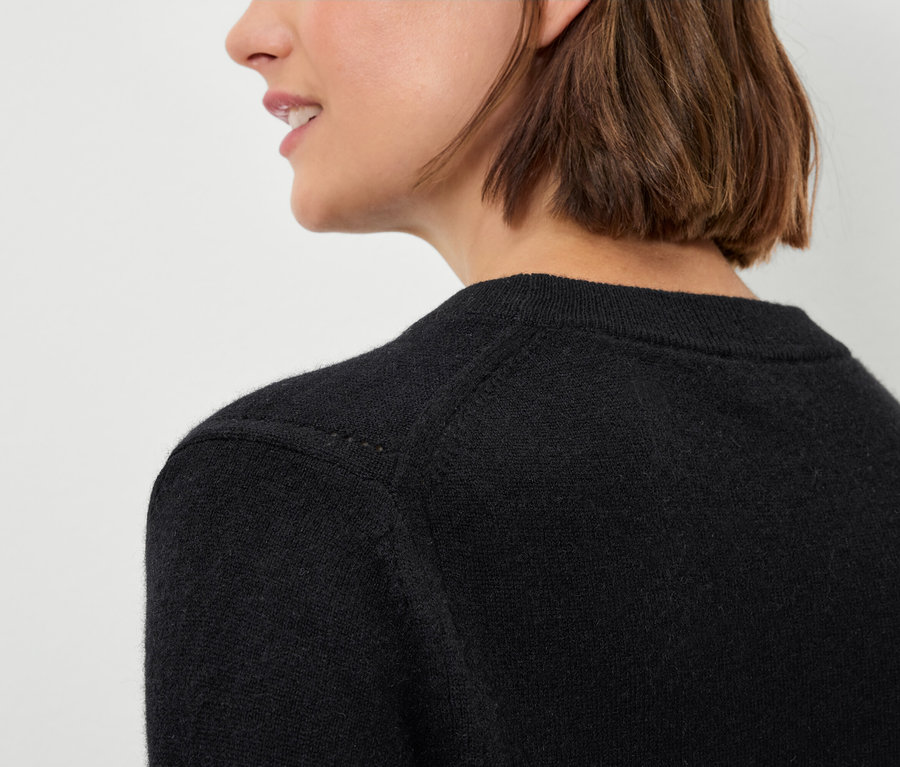 Detailansicht eines schwarzen Damenpullovers an einer Frau mit braunen Haaren.