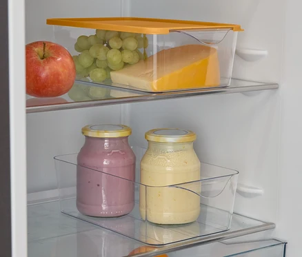 Ein offener Kühlschrank mit Apfel, Trauben, Käse, zwei Smoothie-Gläsern, einer Orange und Limetten.