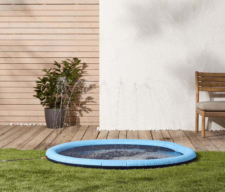 Auf Rasen steht eine blaue Hunde-Wasserspielmatte, aus der Wasser spritzt.