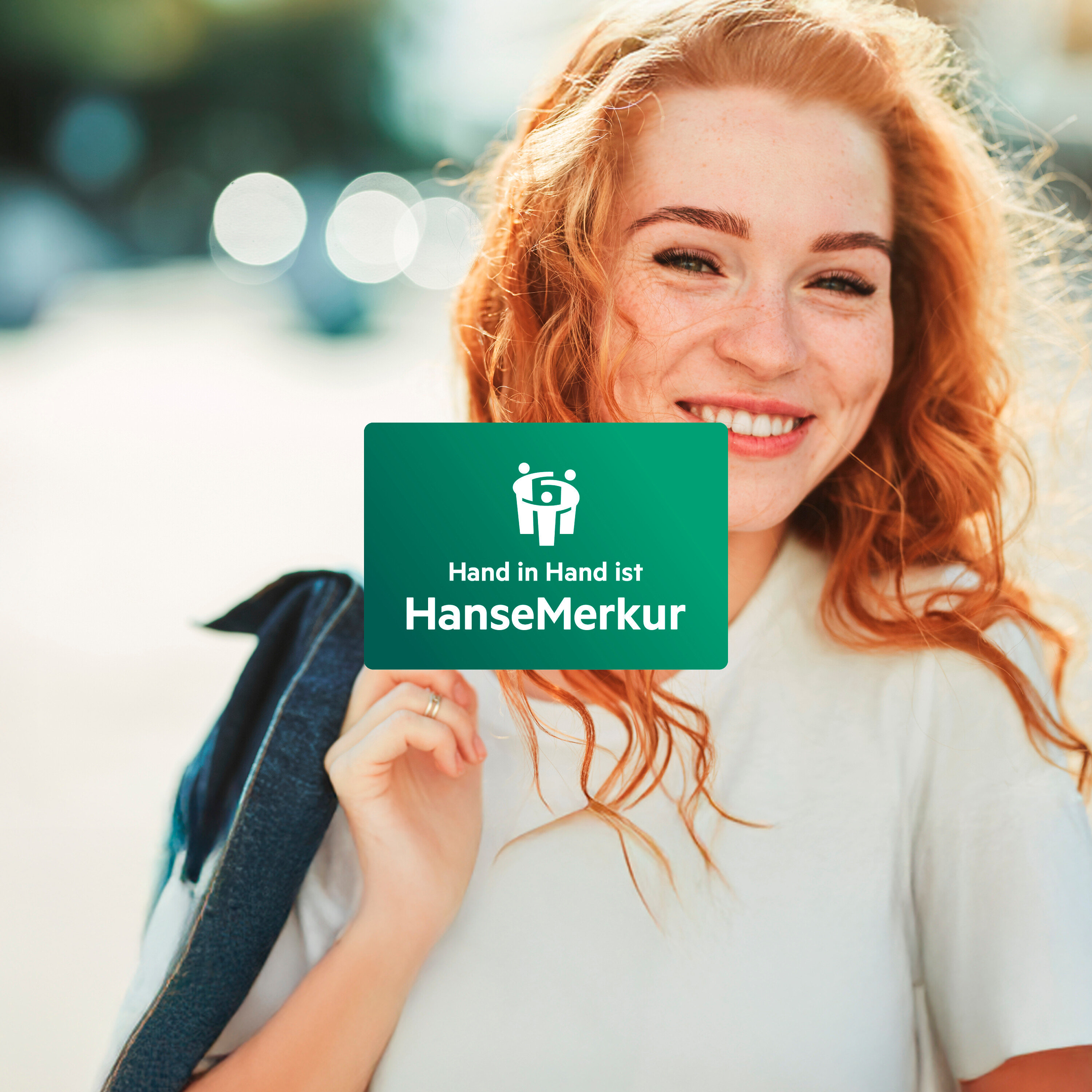 Eine lächelnde rothaarige Frau hält eine grüne Karte mit dem Logo und dem Schriftzug HanseMerkur.