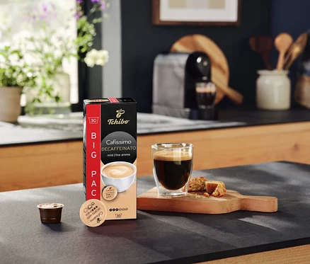 Auf einer Küchentheke stehen eine Packung Cafissimo Decaffeinato Kapseln, eine Tasse Kaffee und eine Kapsel.