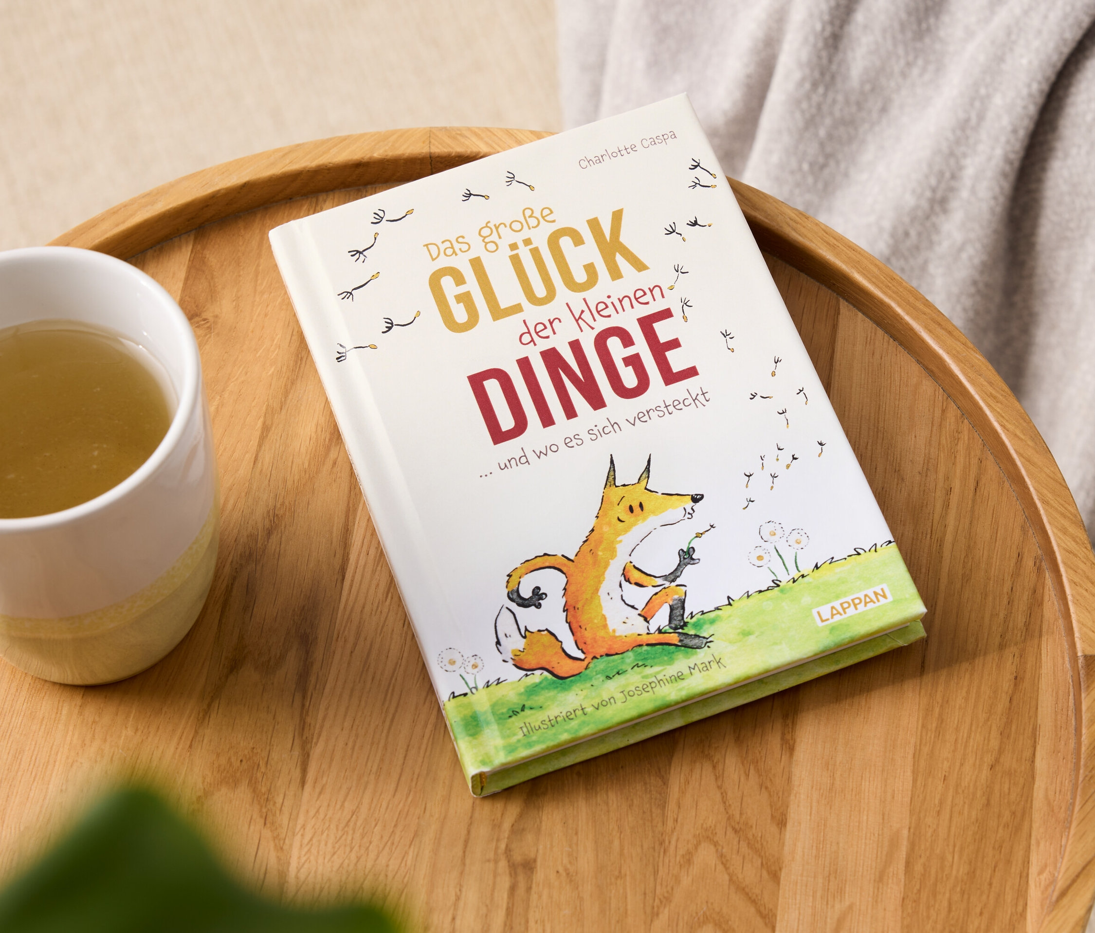 Buch "Das große Glück der kleinen Dinge" und eine Tasse Getränk auf einem Holztablett.
