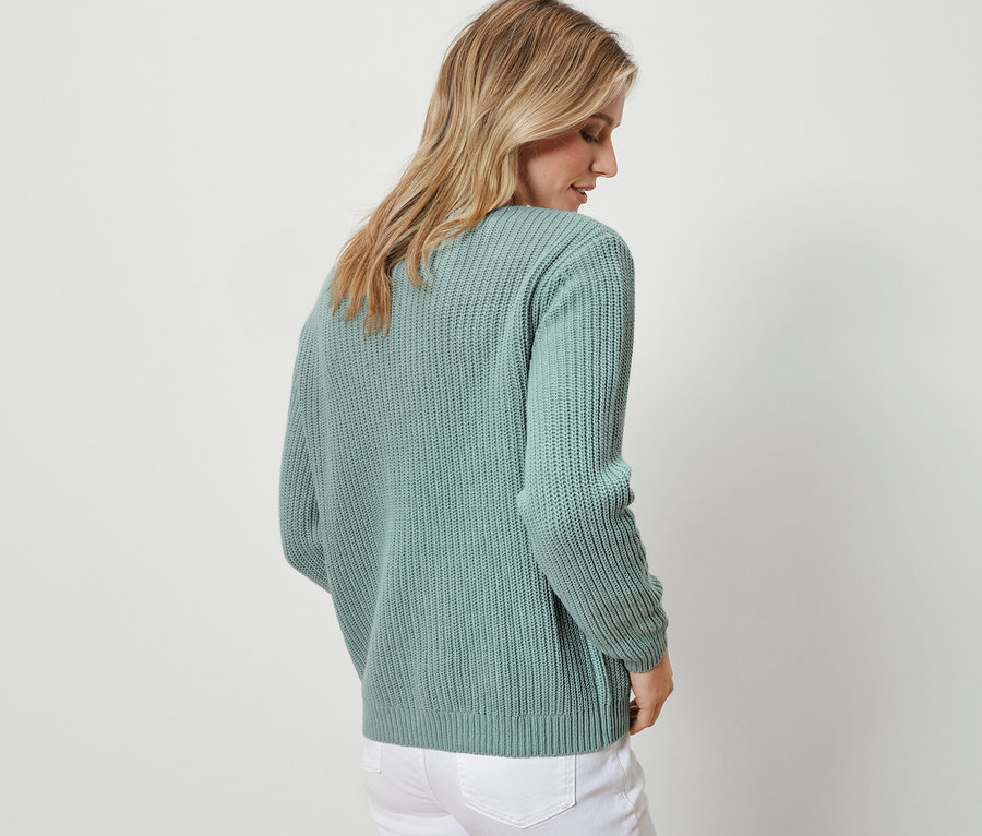 Frau von hinten trägt einen salbeifarbenen Grobstrick-Cardigan und weiße Jeans.