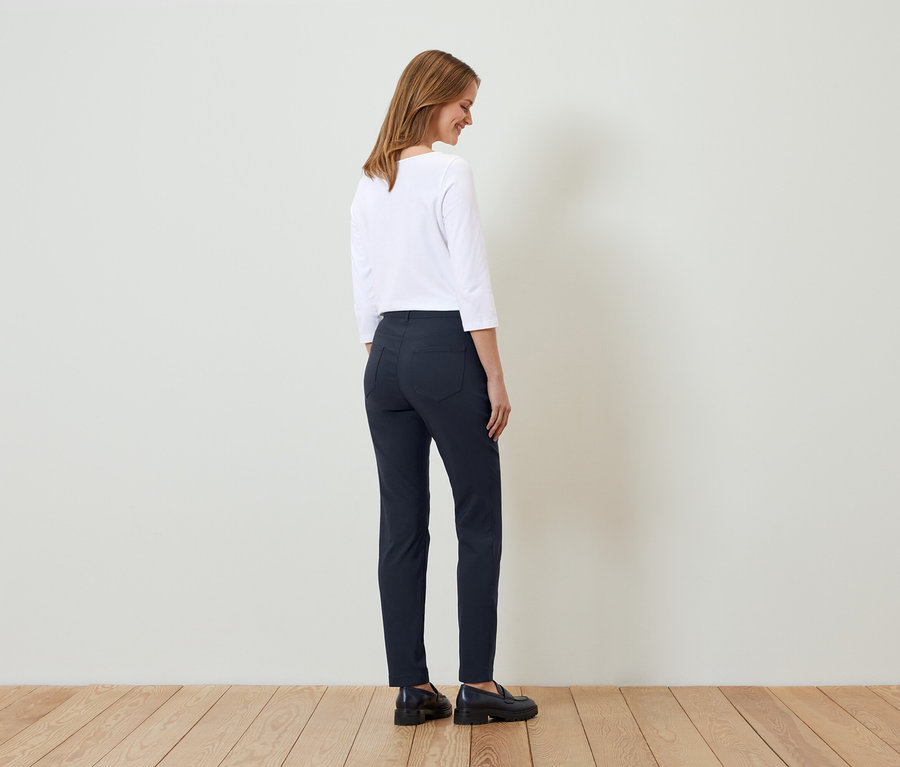 Frau posiert in weißem Oberteil und dunkelblauer Hose.