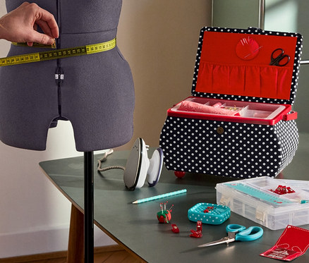 Frau misst die Taille an der Prym Multi-Schneiderbüste »Prymadonna« ab. Daneben: Prym Nähkorb »Polka Dots«, Prym Mini-Dampfbügeleisen, Prym Starter-Set Nähen »Love«.