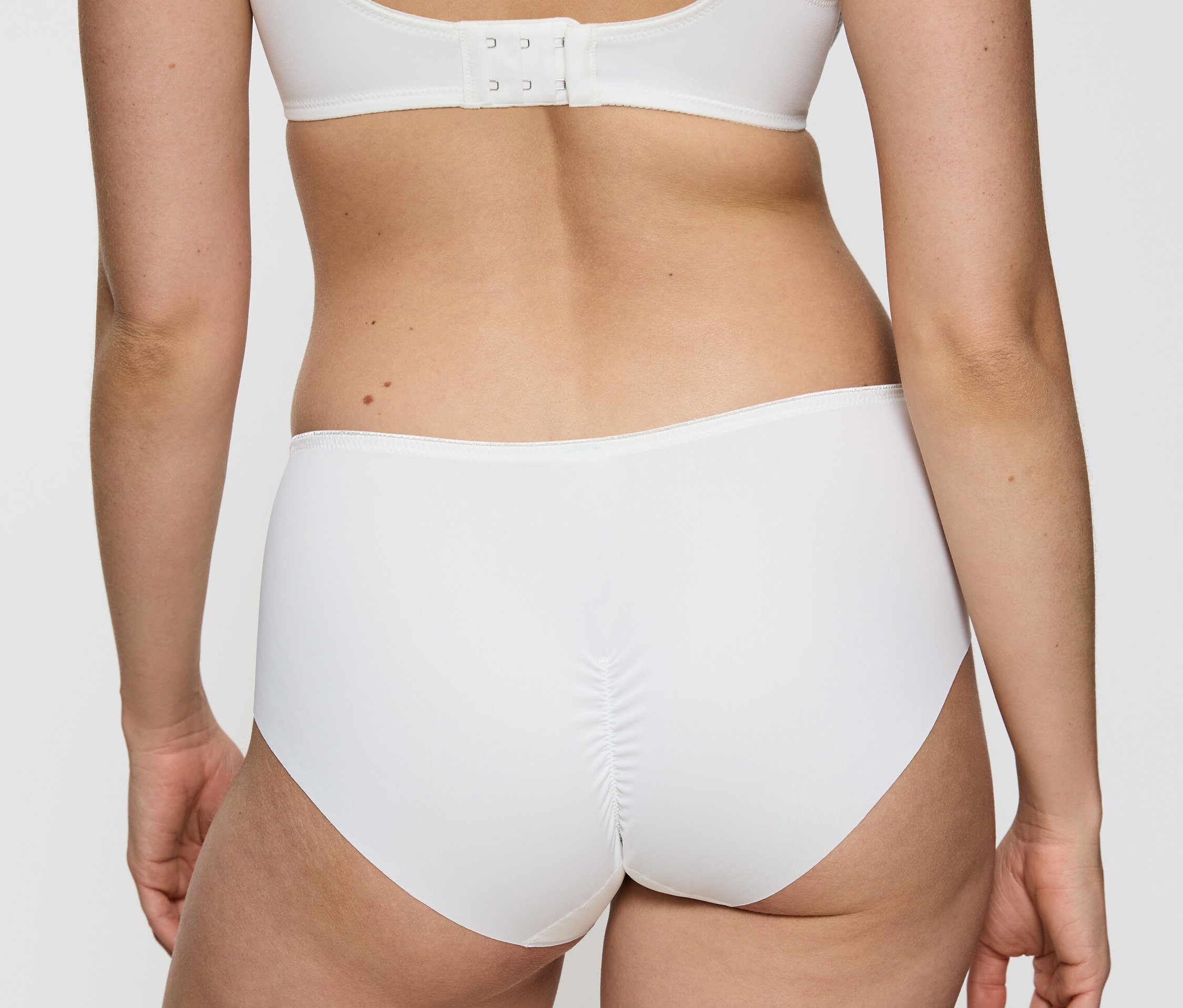 Rückansicht einer Frau, die einen weißen Triumph Essential »Minimizer Hipster X«, Vanille und einen weißen BH trägt.