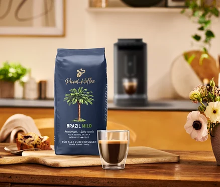 Eine Packung Tchibo Privat Kaffee Brazil Mild, eine Tasse Espresso und ein Stück Kuchen auf einem Holztisch.