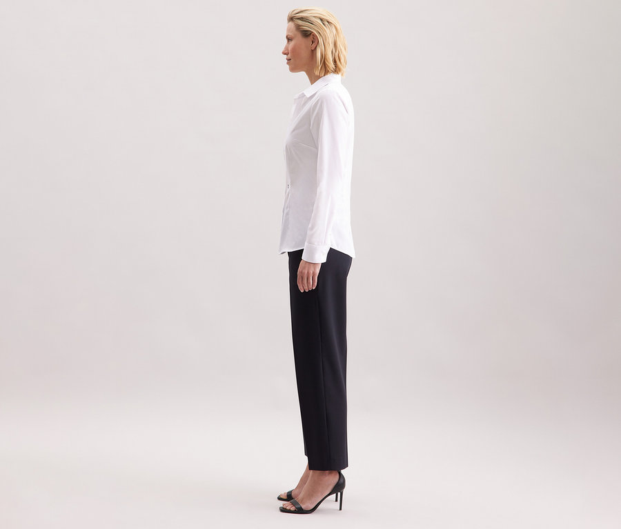 Frau im Profil, trägt eine weiße Seidensticker Bluse Slim Fit non iron, kombiniert mit einer dunklen Hose und schwarzen High Heels.