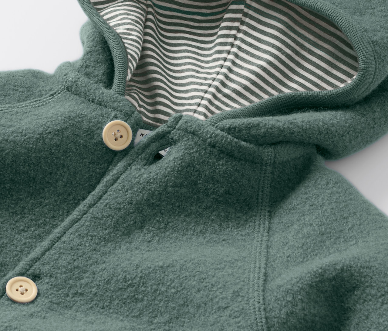 Detailansicht eines Baby-Walkoveralls mit Merinowolle, der mit Knöpfen geschlossen wird und eine Kapuze mit gestreiftem Futter hat.