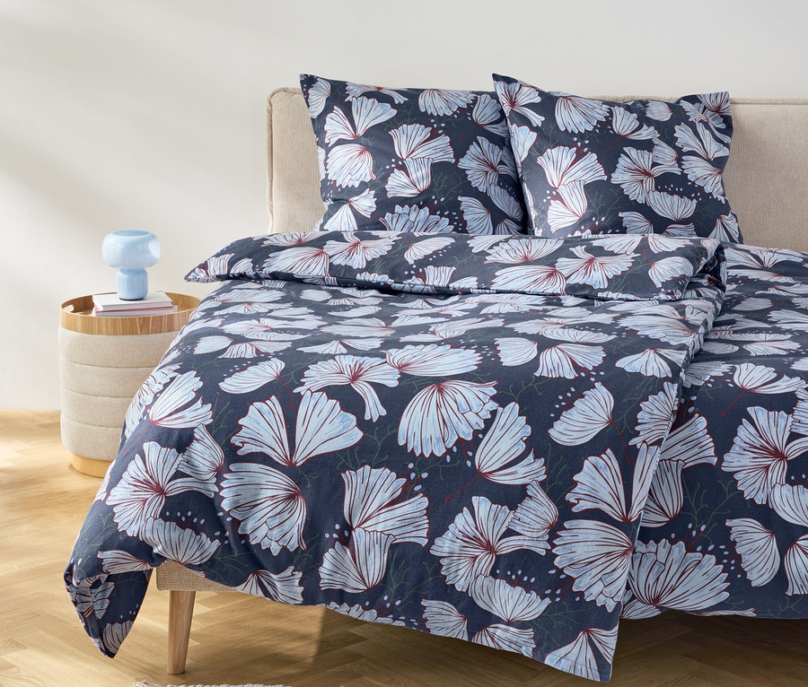 Bett mit marineblauer Bettwäsche mit Blumenmuster und zwei Kissen auf einem beigen Kopfteil.