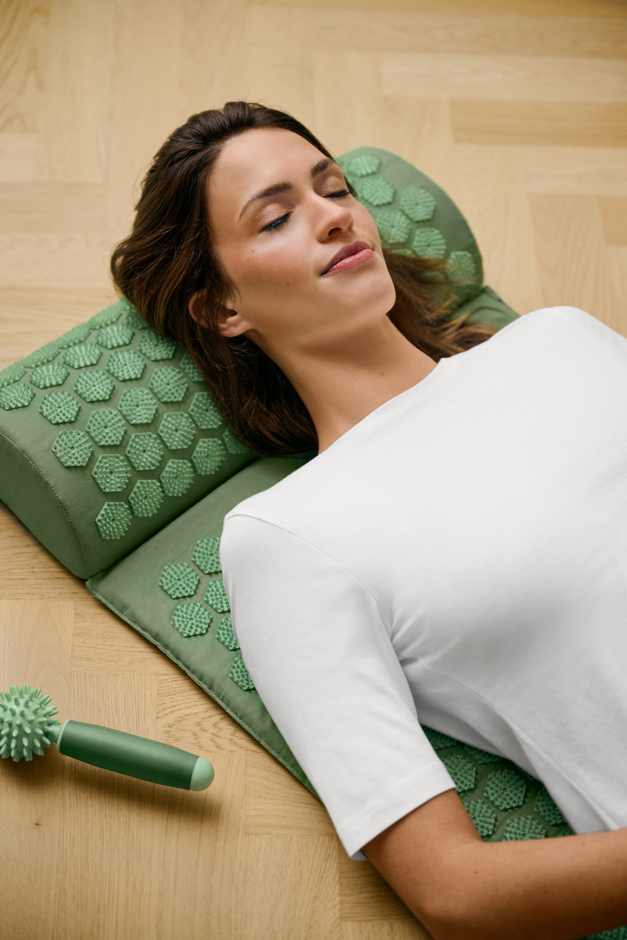 Frau liegt auf einer grünen Akupressurmatte und trägt ein weißes Basic Halbarmshirt.