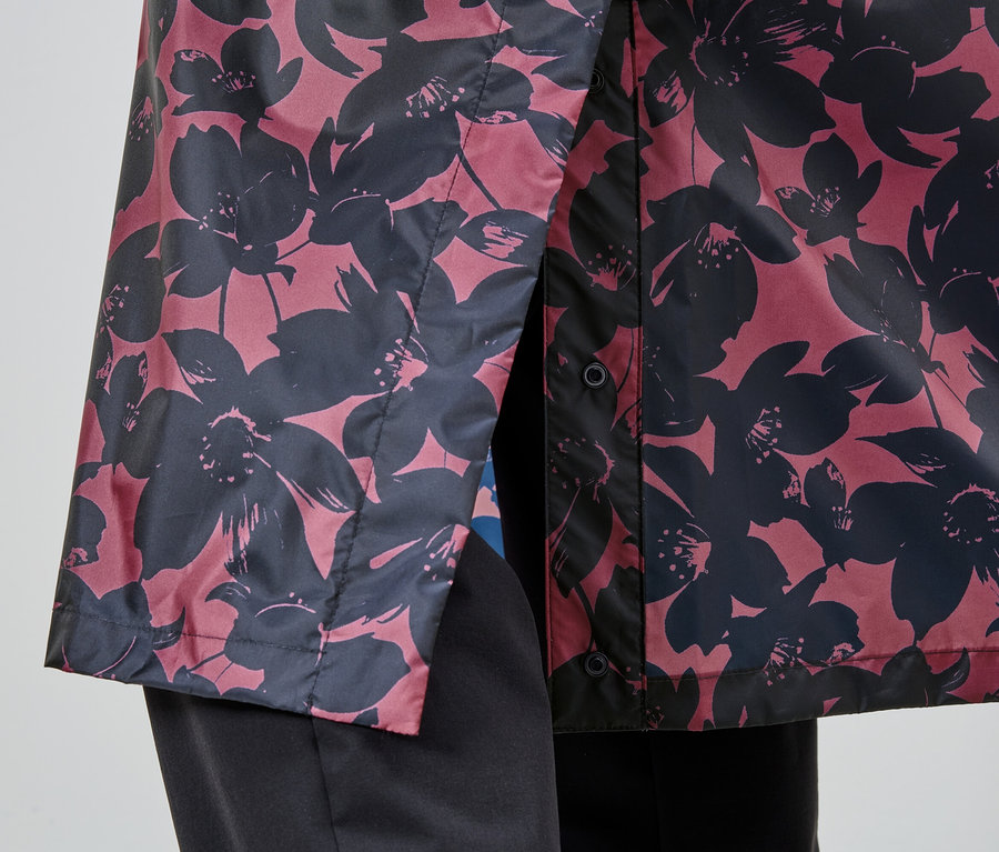 Nahaufnahme einer Person, die eine rosafarbene Jacke mit schwarzem Blumenmuster und schwarze Hosen trägt.