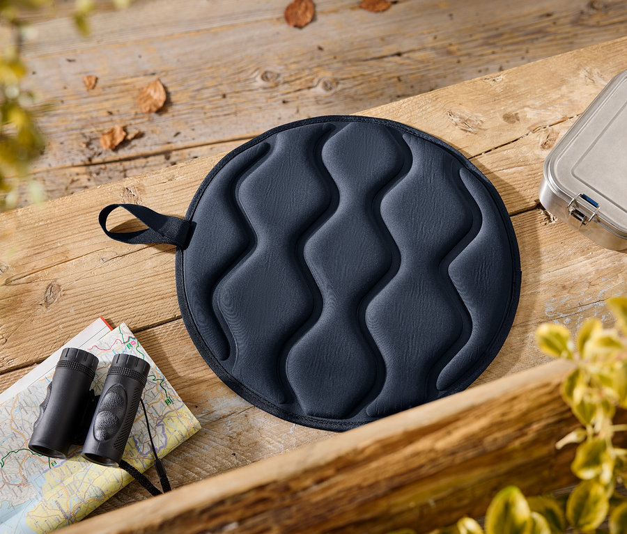 Auf einem Holztisch liegen ein blaues Sitzkissen, ein Lunchbehälter, ein Blatt mit Karte und ein Fernglas.
