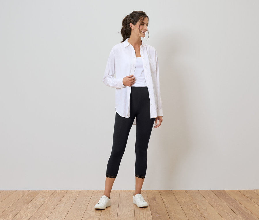 Frau mit weißem Hemd, Tanktop, schwarzen Leggings mit Spitze und weißen Turnschuhen.