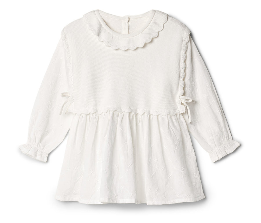 Ein weißes, langärmliges Kleid mit Rüschenkragen liegt auf einem weißen Hintergrund.
