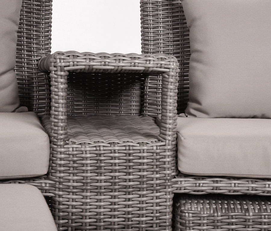 Nahaufnahme eines grauen Korbsessels mit hellgrauen Kissen und integriertem Beistelltisch.