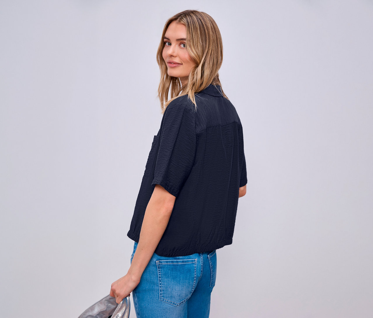 Frau blickt über die Schulter und trägt eine Street One Hemdbluse und Jeans.