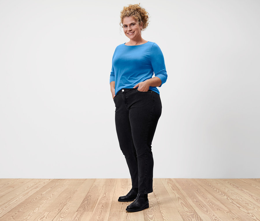 Frau steht und trägt ein blaues Shirt mit 3/4-Arm.