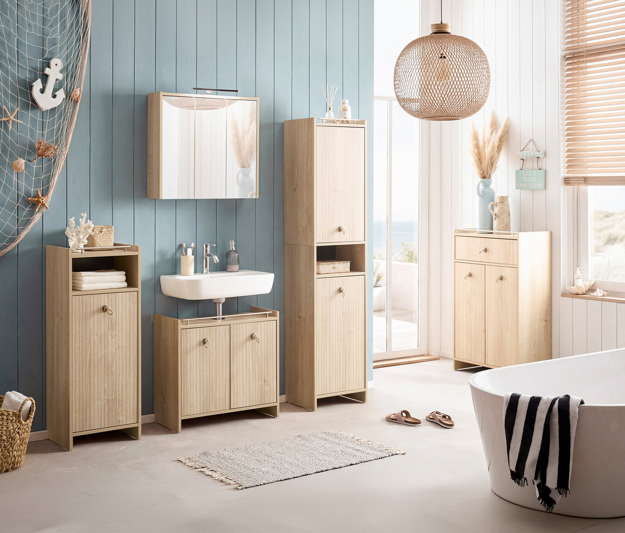 Badezimmer mit Waschtisch, Spiegelschrank und Hochschrank in Holzoptik. Badewanne mit Handtuch und Deko-Elementen. Fenster mit Meerblick.