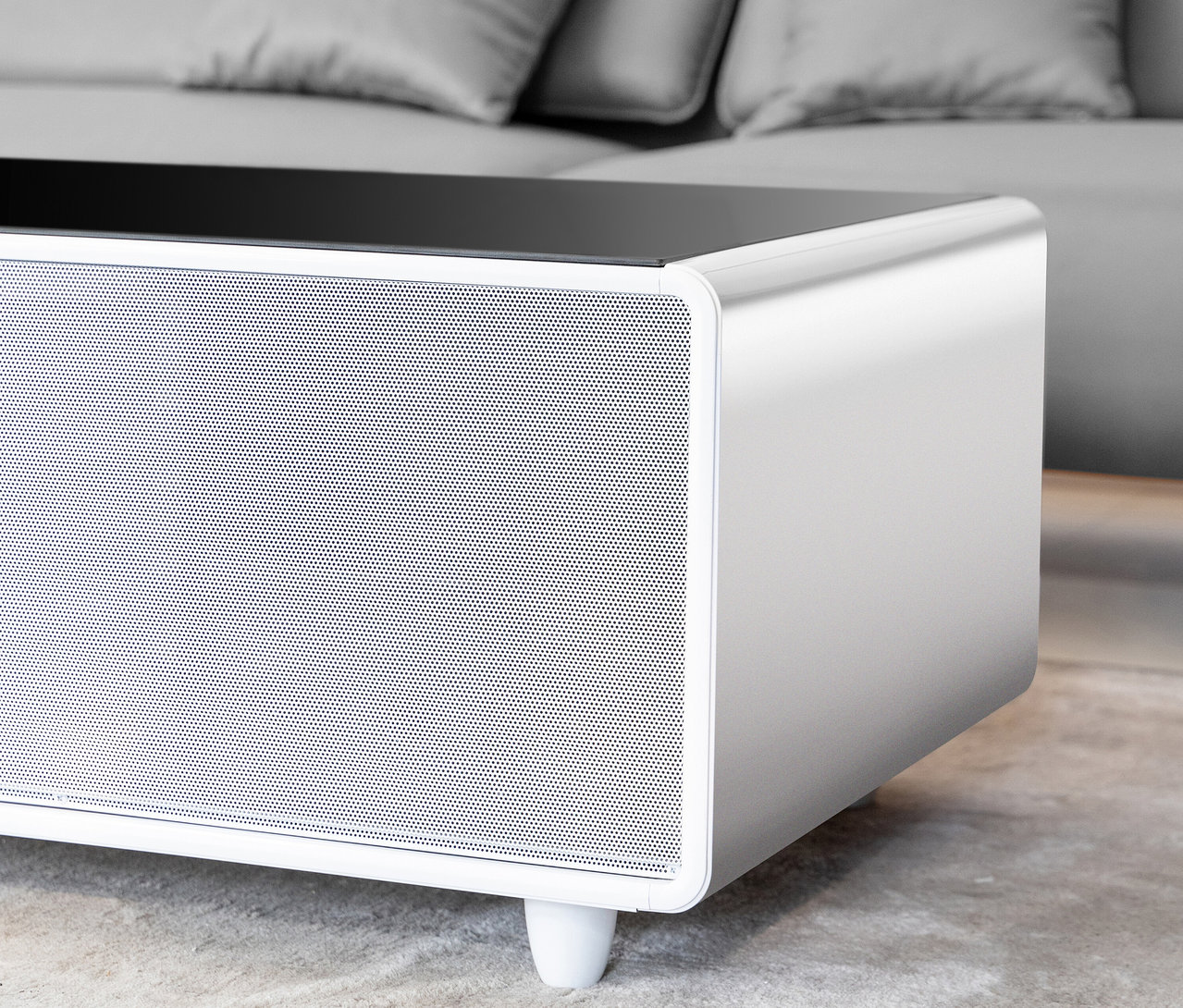 Weißer Caso Sound & Cool Tisch mit Lautsprecher und Glasplatte vor grauem Sofa.