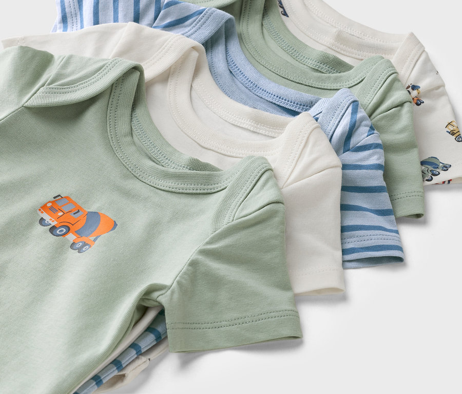 Nahaufnahme von kurzärmeligen Babybodys in verschiedenen Farben und Mustern, darunter ein grüner Body mit einem Betonmischer-Motiv.
