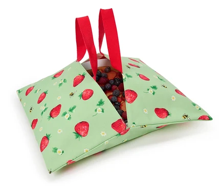 Erdbeerkuchen in einer grünen Stofftasche mit Erdbeermuster und roten Henkeln.