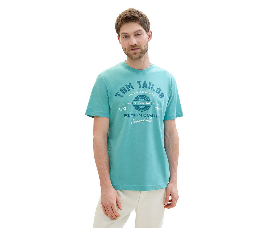 Mann trägt ein Tom Tailor T-Shirt mit Logo in Meadow Teal und helle Hose.