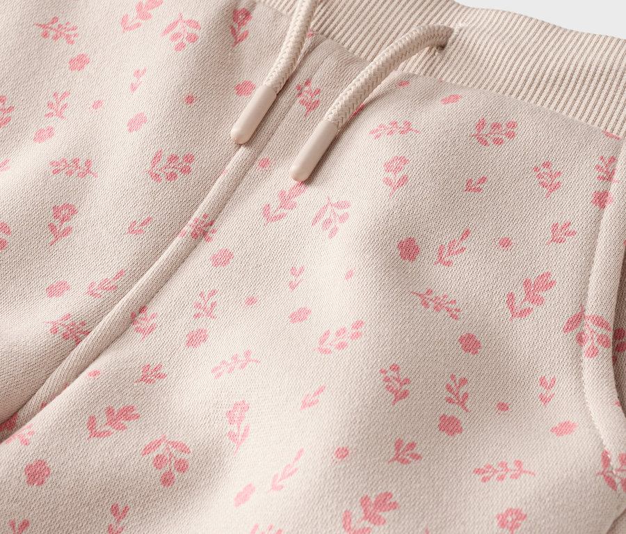 Nahaufnahme einer beigen Hose mit rosa Blumenmuster, Kordelzug und Tasche.