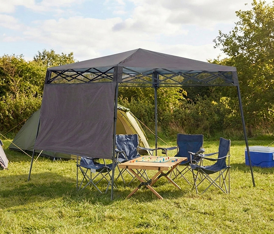 Auf einer Wiese stehen ein grauer Pavillon, vier blaue Campingstühle und ein Holztisch mit einem Brettspiel.
