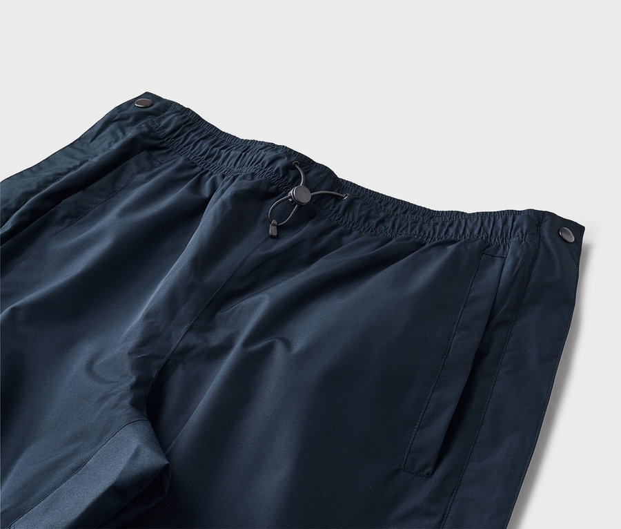 Nahaufnahme einer marineblauen Hose mit elastischem Bund, Kordelzug und Seitentasche vor einem neutralen Hintergrund.