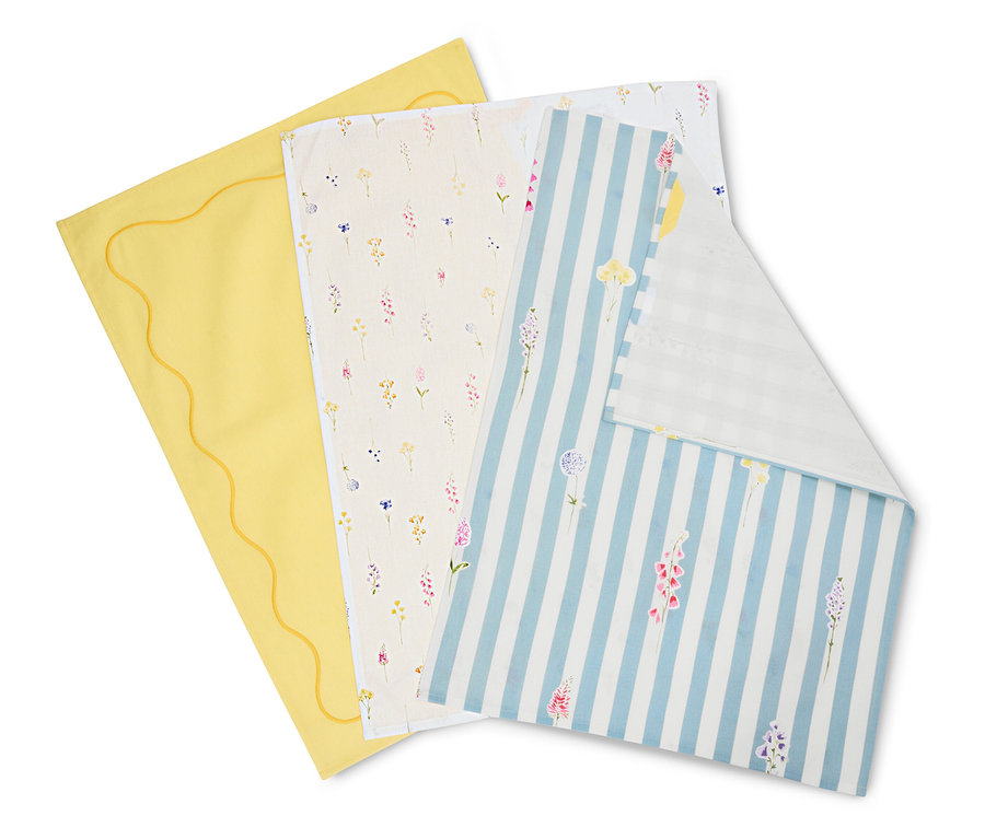 Drei Tücher liegen übereinander: ein gelbes mit gewelltem Rand, ein cremefarbenes mit Blumenmuster und ein blau-weiß gestreiftes mit Blumen.