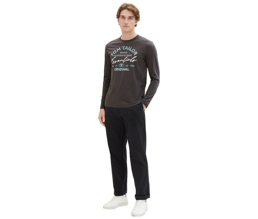 Mann in dunklem Tom Tailor Longsleeve mit Logo und dunkler Hose, stehend.