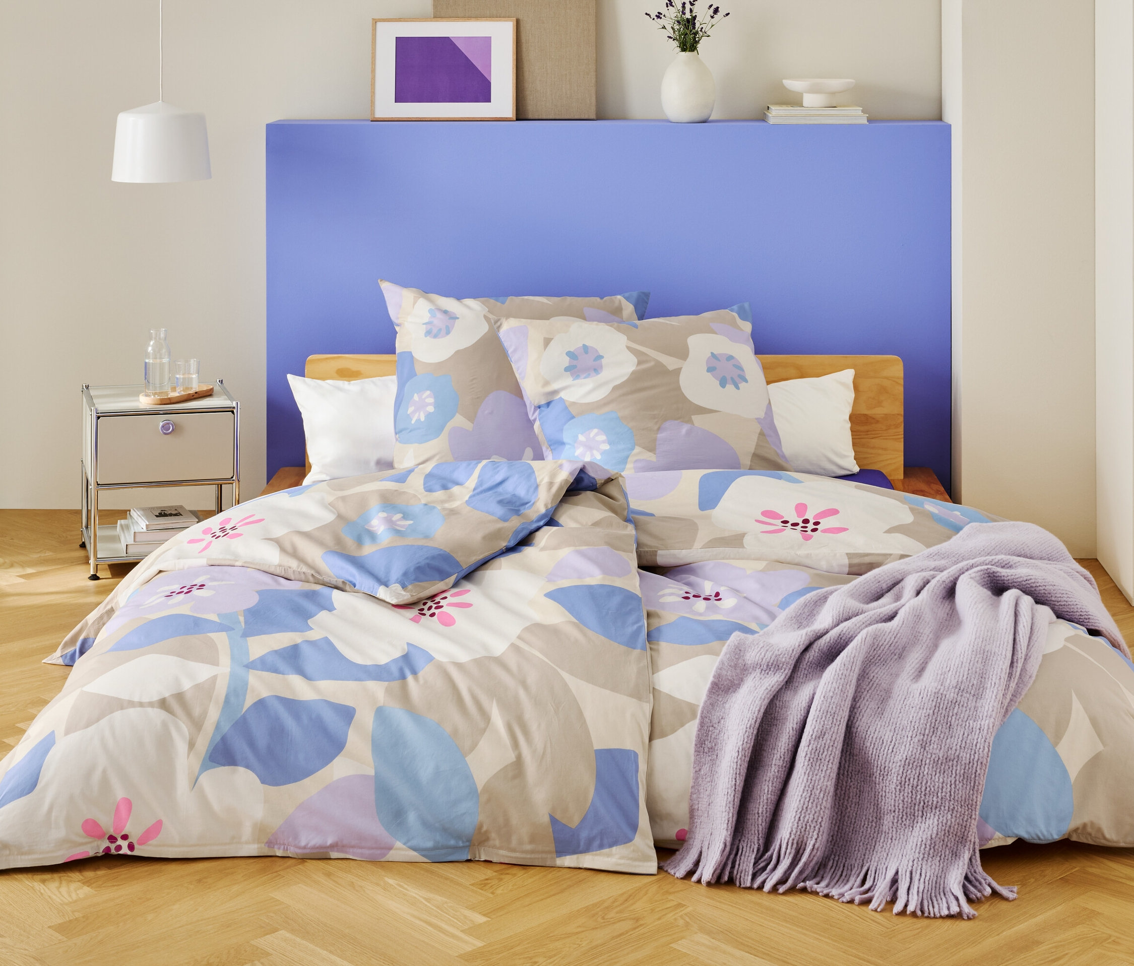 Ein Schlafzimmer mit einem Bett, das mit floraler Bettwäsche und einer lila Decke bedeckt ist.