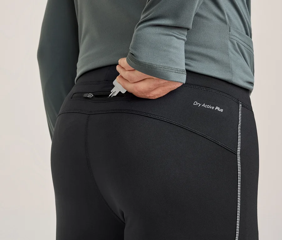 Eine Person von hinten steckt Schlüssel in die Reißverschlusstasche einer schwarzen Sporthose. Die Hose hat den Schriftzug „Dry Active Plus“ und einen reflektierenden Streifen.