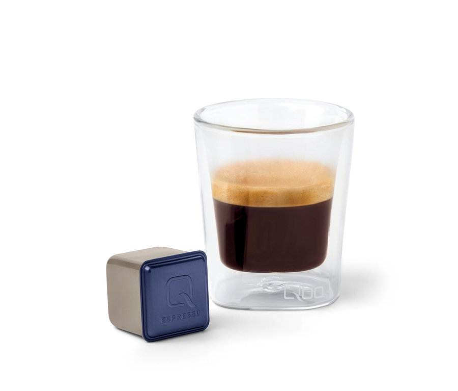Eine Qbo Espresso INDIAN KAVERI Kapsel neben einem Glas Espresso.