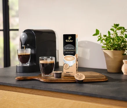 Kaffeemaschine gießt Kaffee in ein Glas neben einer Packung Cafissimo Decaffeinato - entkoffeiniert - 10 Kapseln.