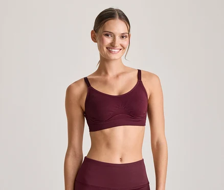 Lächelnde Frau in einem bordeauxroten Sport-BH und passenden Leggings, blickt in die Kamera.