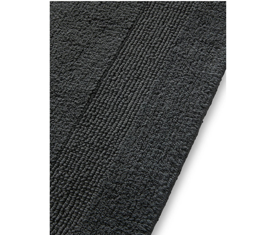 Nahaufnahme einer dunkelgrauen Badematte mit einer plüschigen Textur und einem diagonal gerippten Bereich.