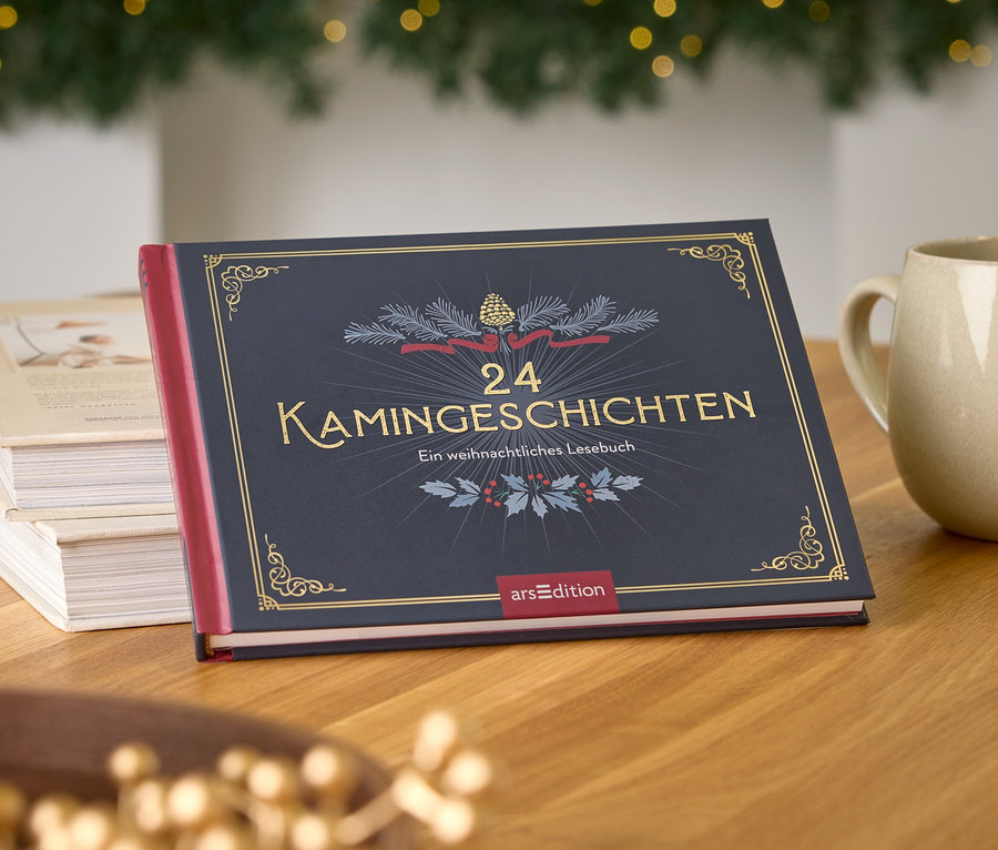 Buch "24 Kamingeschichten" auf einem Holztisch neben einer Tasse und einer Vase, im Hintergrund ein Weihnachtsbaum.