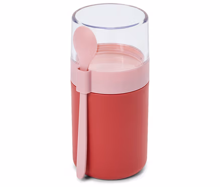 Ein roter Lebensmittelbehälter mit einem rosafarbenen Band und einem transparenten Deckel, an dessen Seite ein rosafarbener Löffel befestigt ist.