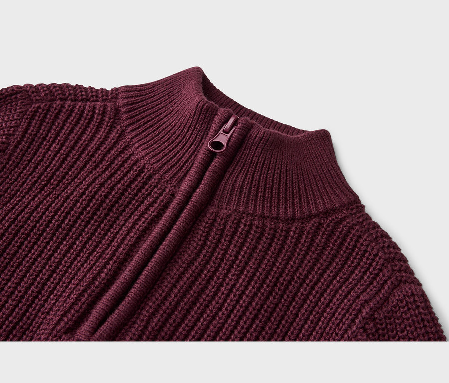 Nahaufnahme eines burgunderroten Strickpullovers mit Rippenstruktur, Reißverschluss und Stehkragen.