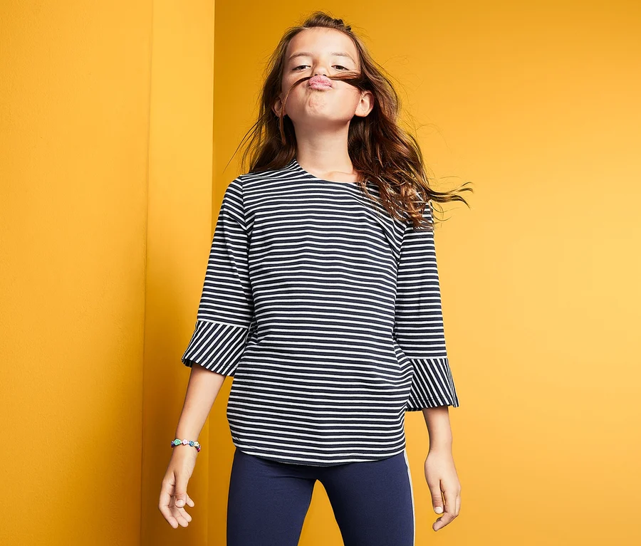 Mädchen mit Streifenshirt steht vor gelbem Hintergrund.