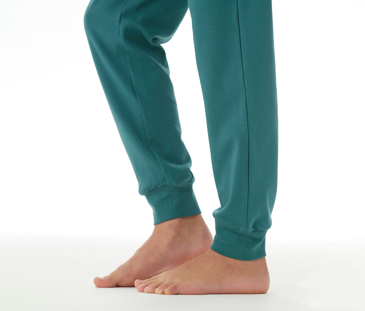 Kinderbeine in einer petrolfarbenen SCHIESSER Kinder-Interlock-Pyjamahose mit Bündchen, die Füße sind barfuß.