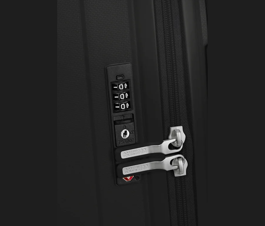 Nahaufnahme eines schwarzen American Tourister Rejoy Spinner Koffers, der sein integriertes Zahlenschloss mit "000" und TSA007-Schlüsselloch zeigt. Zwei silberne American Tourister Reißverschlussgriffe sind im Schloss gesichert, neben einem schwarzen Reißverschluss.