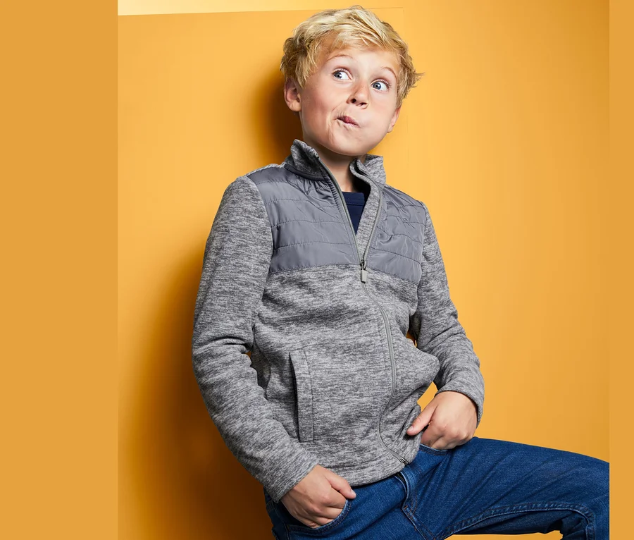 Junge posiert in Hybrid-Fleecejacke vor gelbem Hintergrund.
