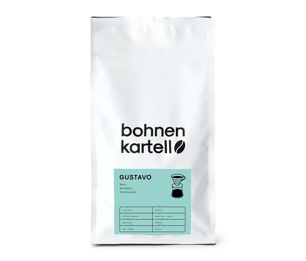 Ein weißer Beutel bohnenkartell Gustavo Filterkaffee, 1 kg Ganze Bohne, mit einem hellblauen Etikett, das Geschmacksnoten wie Nuss, Karamell und Schokolade sowie eine Pour-over-Kaffeemaschine zeigt.